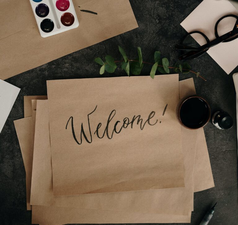 "Welcome!" written on brown paper, amid other items on a desk.